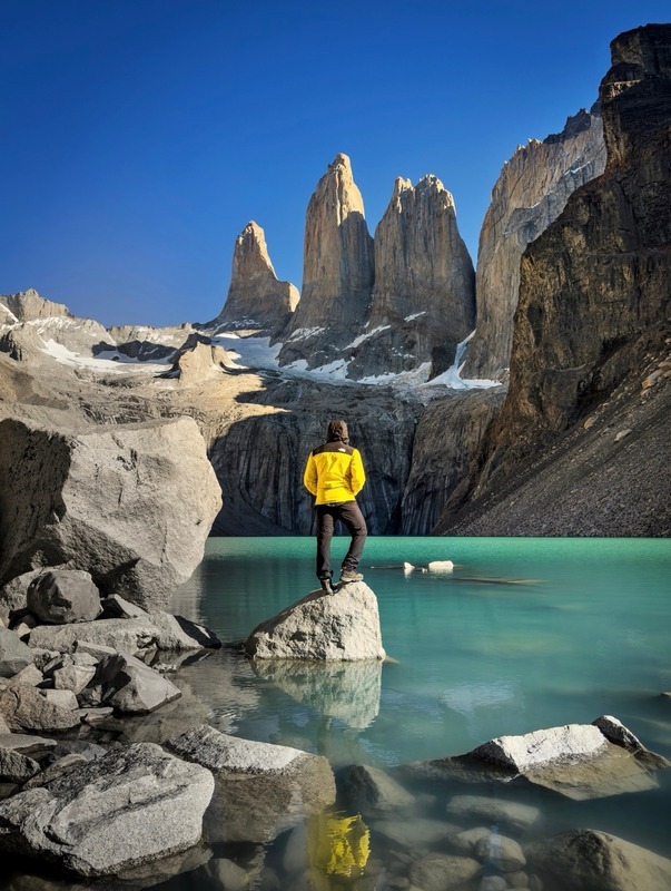 Viajero sobre una roca frente a las Torres del Paine y su laguna turquesa